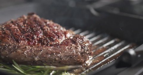 Slide slow motion shot of cooking rib eye steak with herbs on grill pan, 4k 60fps prores footage