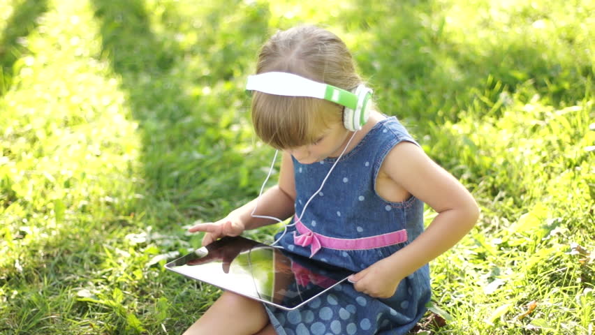 Laughing little girl in headphones is online with a Tablet PC
