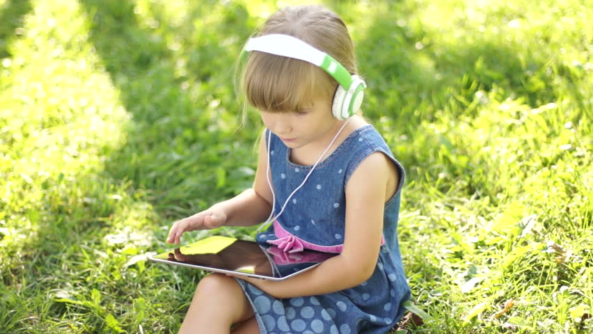 Little girl in headphones is online with a Tablet PC
