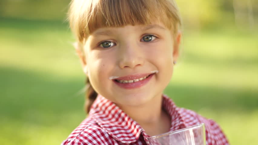 Close-up portrait of smiling girl drinking milk outdoors. Milk mustache.

