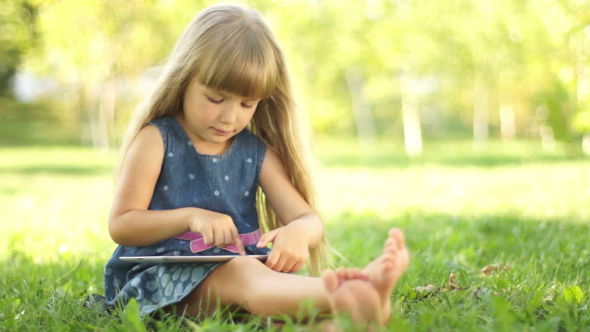 Girl with a tablet pc sitting on the grass. Thumbs up. Ok

