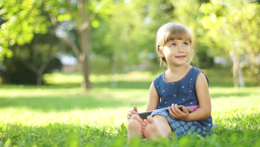 Happy child with a tablet pc sitting on the grass. Thumbs up. Ok
