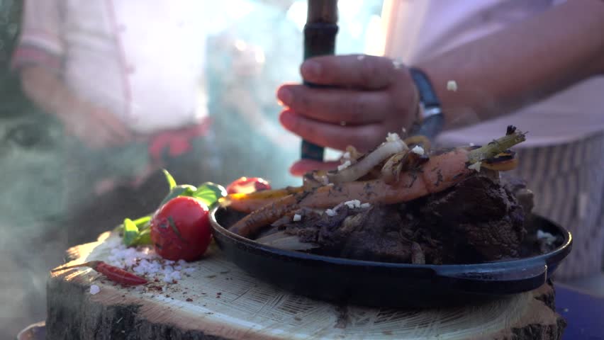 Cook prepares a dish of veal meat with tomatoes and greens