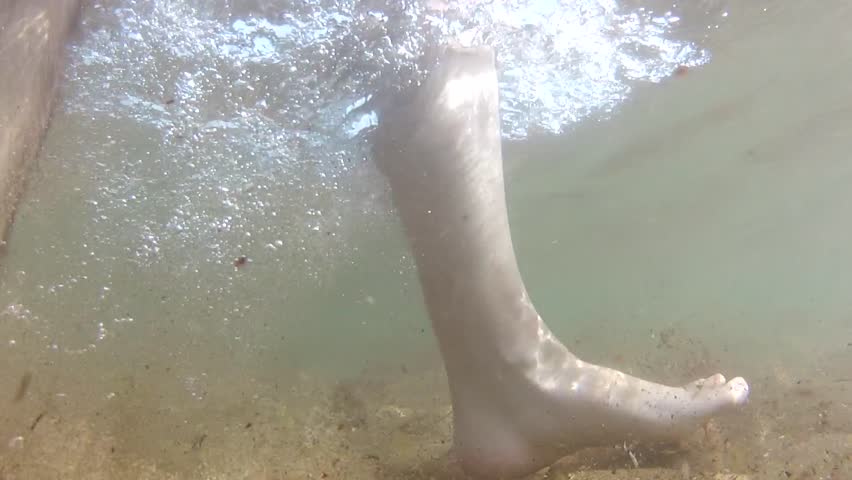 Underwater shot of feet walking along the ocean floor.