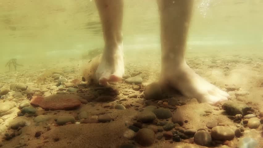 Underwater shot of feet walking along the ocean floor.