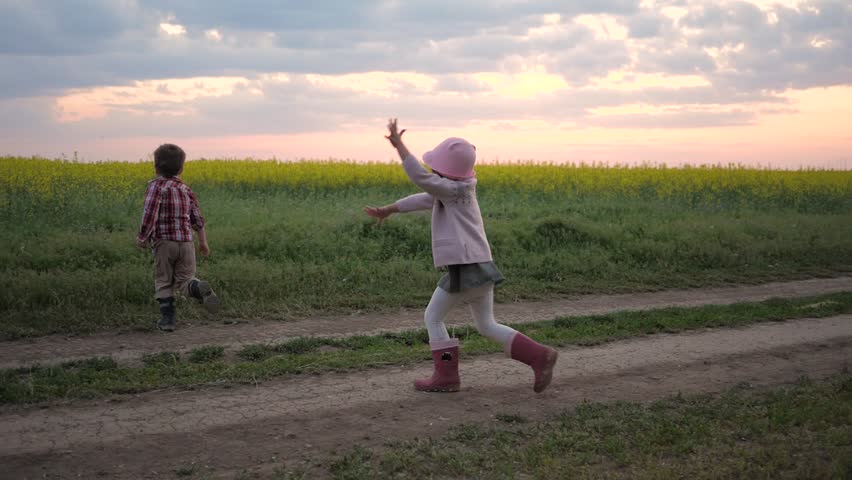 kids are playing in catch-up outdoors, happy children are having fun and laughing, sisters and brother running on field road at sunset 