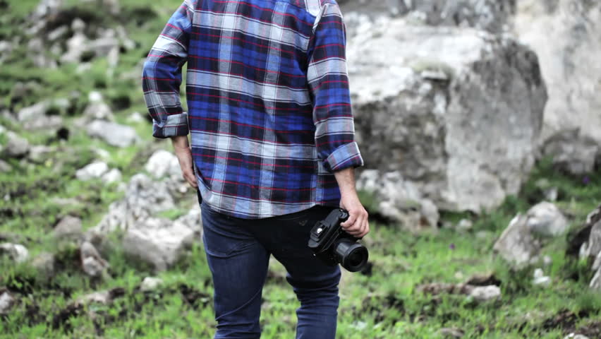 Photographer takes pictures of wildlife in the mouintains. Traveler dressed as lumberjack style, walking and taking photo at beautiful rocky place.