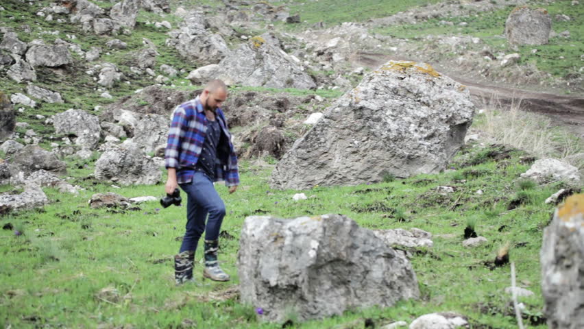 Photographer takes pictures of wildlife in the mouintains. Traveler dressed as lumberjack style, walking and taking photo at beautiful rocky place.