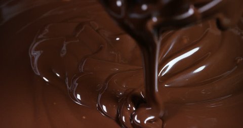 Delicious brown chocolate is prevented by a machine at a professional factory making sweets, on a chocolate background. Concept: the production of sweetness, cream, chocolate, delicious air, gourmet.