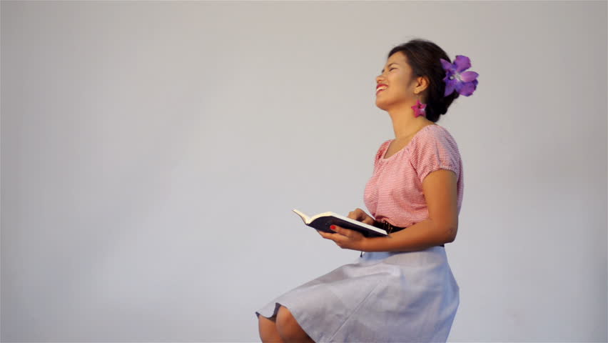 Young Asian woman bursts out laughing as she reads a book/the bible.