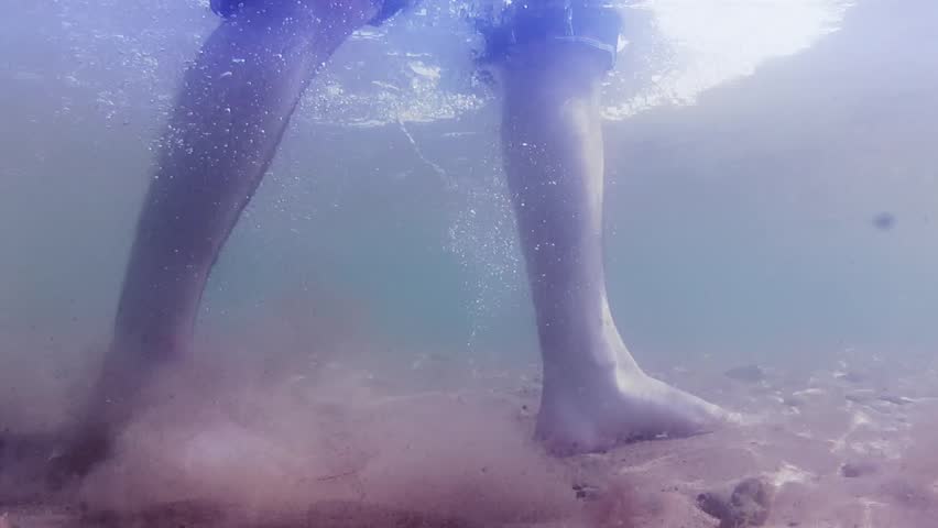 Underwater shot of feet walking on sandy ocean beach