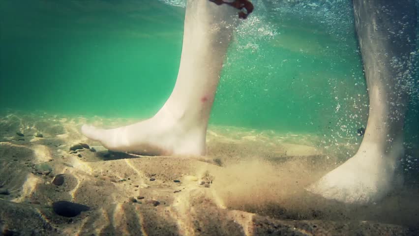Underwater shot of feet walking on sandy ocean beach