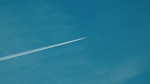 Flying jet airliner leaving contrain in the blue sky. 4K telephoto lens clip