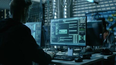 Young Hacker Breaks into Corporate Data Servers from His Underground Hideout. Place Has Dark Atmosphere, Multiple Displays, Cables Everywhere. Shot on RED EPIC-W 8K Helium Cinema Camera.