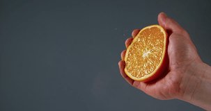 Hand of Man Squeezing Orange against Black Background, Slow Motion 4K