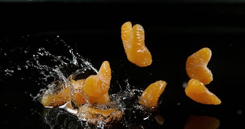 Clementines, citrus reticulata, Fruits falling on Water against black Background, Slow Motion 4K