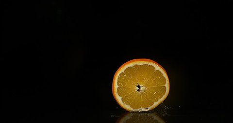 Orange, citrus sinensis, Slice rolling on Water against Black Background, Slow Motion 4K