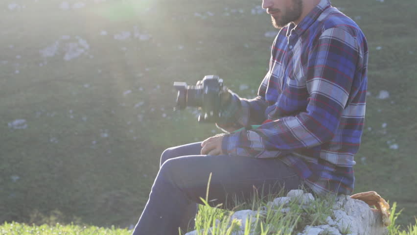 Photographer sitting and changing lenses on professional camera outdoor. shooting against the sun with beautiful sunrise natural light.