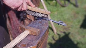 Smith Connects Metal Grey Rods. he Holds Them by Means of a Rusty Metal Nippers. a Old Forge Hammer Lies on a Massive Anvil. the Smith Bends the Rods With His Help. Video is Filmed in Mode of a