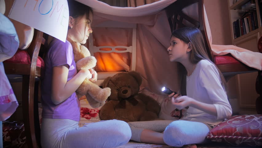 Two girls telling scary stories in tepee tent in bedroom at night