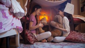 4k video of two girls in pajamas playing with teddy bear in selfmade tent at bedroom