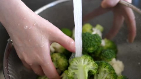 Slow motion of woman washing broccoli in a colander under tap water