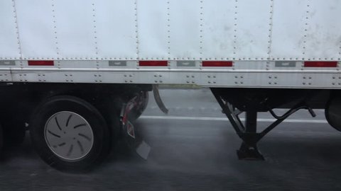 SLOW MOTION CLOSE UP: Detail of a raindrops spraying from the chassis and tires of a semi truck driving along the wet highway in bad weather condition during rainy storm. Lorry hauling freight in rain