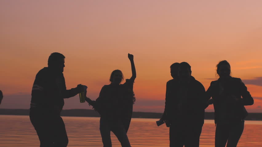 Slow motion of Silhouette group young dancing people have a party at beach on sunset