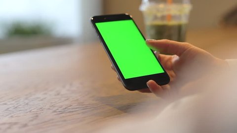 Woman browsing one finger green screen on mobile phone in cafe shop. Handheld video with female and chroma key smartphone display. Used mobile phone for copy past advertising or game design template