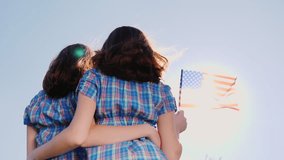 Two female twins with an American flag on a blue sky background. Back view. independence Day