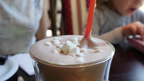 Closeup cacao foam with white marshmallows are stirred with a plastic straw