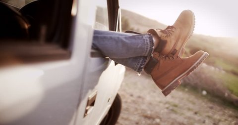 Women legs with boots sticking out of a car during camping trip in the country
