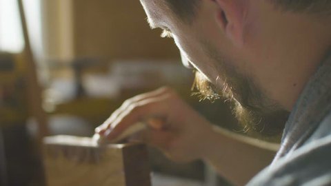 close up concentrated carpenter woodworker rubs lacquer in wooden plank in backlight