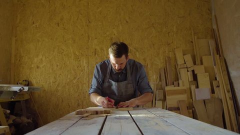 20s bearded carpenter drawing in workshop in sunny day