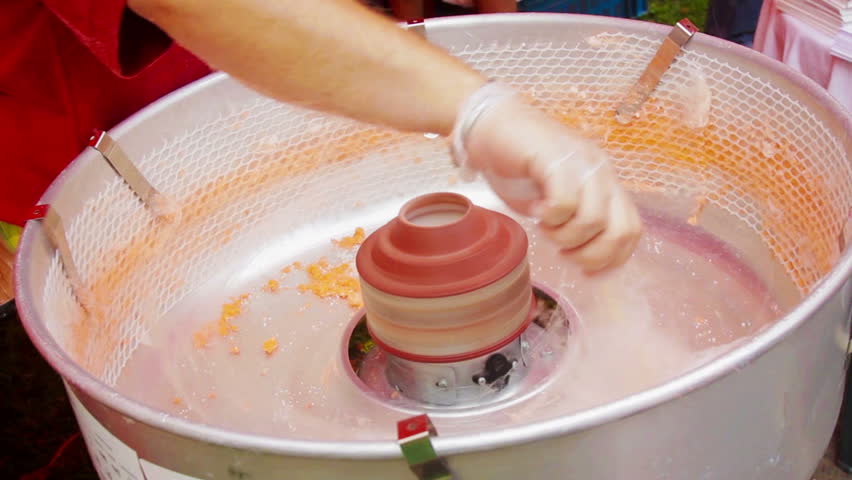 Working man making orange cotton candy during holiday festival (close-up on
