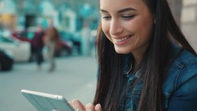 Beautiful smiling woman using tablet device while sitting on stairs on the street. Woman reading, tapping on touchscreen, watching videos. Close up