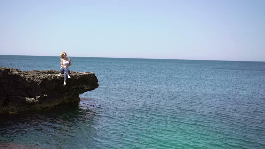 Young blonde woman on rocks near sea at windy day