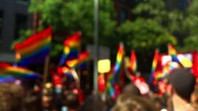Rainbow flags flying on a float and in the hands of spectators on the sidelines in a defocus view of a summer gay pride parade in Greenwich Village, New York City