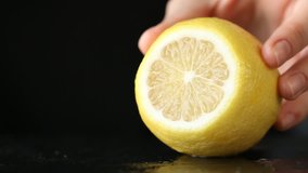 Close-up of woman hand cutting lemon on black stone