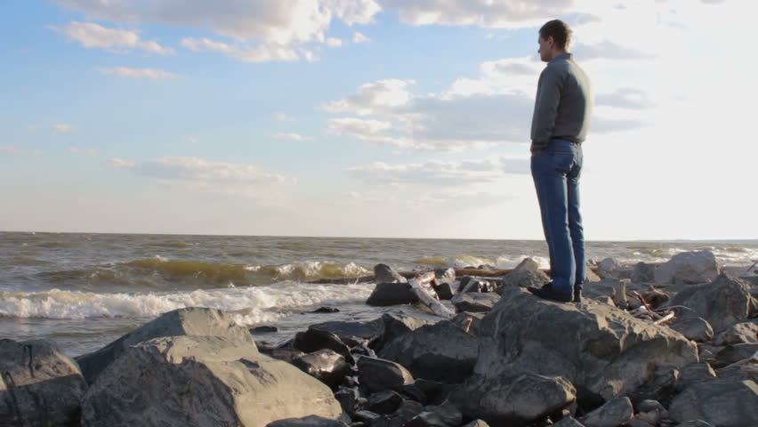 Young businessman standing on a rocky sea shore, enjoying landscape view
