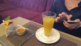Glass of juice and cake on table near hands of woman touching smartphone in cafe close up, mobile phone video.