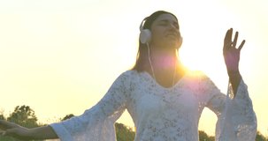 Beautiful girl (woman) walking on a field in a white dress, dancing, listening to music on a nature background. Concept: people enjoy nature, dresses, lifestyle, freedom, ecology, summer, summer day.