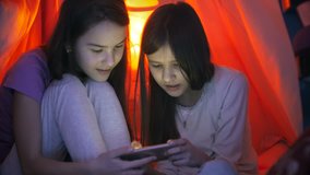 4k footage of two girls in pajamas browsing internet on smartphone under blanket at night