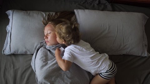 Cute little boy waking up his mother in the morning by kissing her. Flat lay medium shot