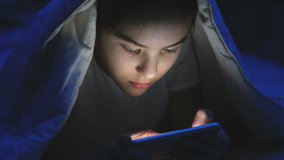 Closeup footage of girl lying under blanket at night and chatting on smartphone