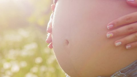 Pregnant woman tummy. Woman's hand caressing her nude pregnant belly. Female hand on tummy of expectant mother at spring outside.