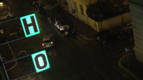 Footage close up from fourth floor looking down out of hotel window on streets during rainy night showing illuminated hotel sign and dark streets cars passing by with lights driving through evening 4k