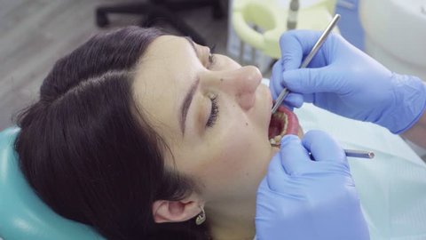 Young female patient in dentist office. Dentist examines the patient teeth at dental chair with open mouth, dental procedure in clinic. Stomatology concept
