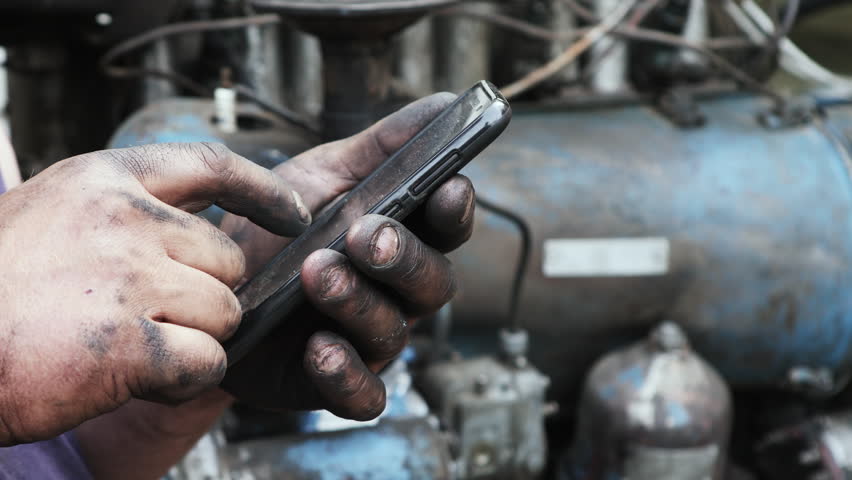 Mobile phone in the hand closeup. Use of the Internet in a mobile phone. A man is looking for information in the phone. Unsanitary conditions, dirty hands in fuel oil. | Shutterstock HD Video #27330895