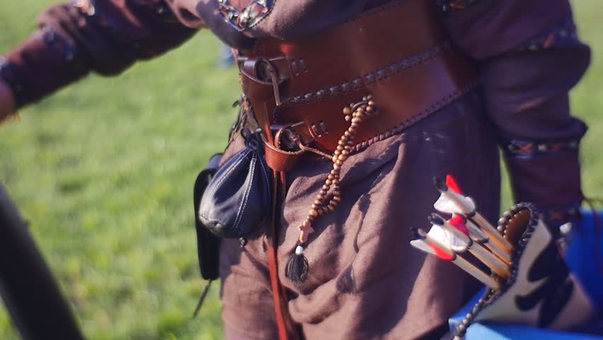 an Archer, Dressed in a Leather Armor, Carries a Trophies. a Small Quiver, Full of Sharp Arrows, Hanging on His Belt. the Archer Goes Along a Field. a Grass Grows on the Field. the Archer is Dressed